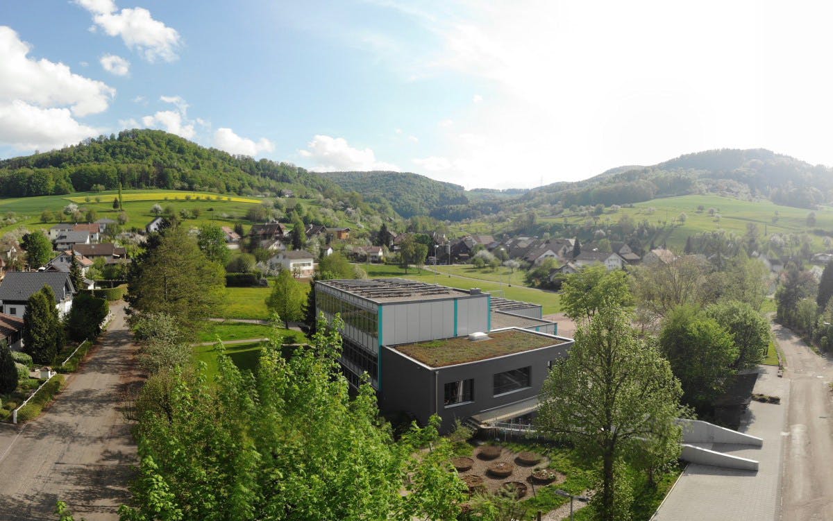 Die Schule Oberhof im Kanton Aargau: mitten im Dorf, eingebettet in eine grüne, hügelige Landschaft mit viel Gestaltungsmöglichkeiten im Aussenraum. Im Vordergrund gut erkennbar: der Nutzgarten mit seinen runden Beeten.
