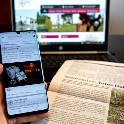 Eine Person hält ein Handy, auf dem ein Zeitungsartikel der Gemeinde Köniz zu sehen ist.