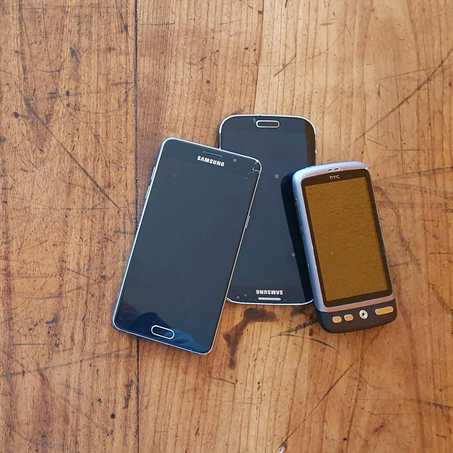 Drei alte Handys liegen auf einem Holztisch.