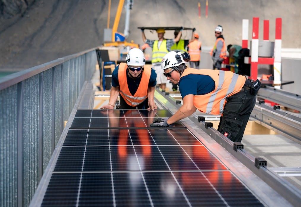 Arbeiter installieren Solarpanels auf einer Staumauer.