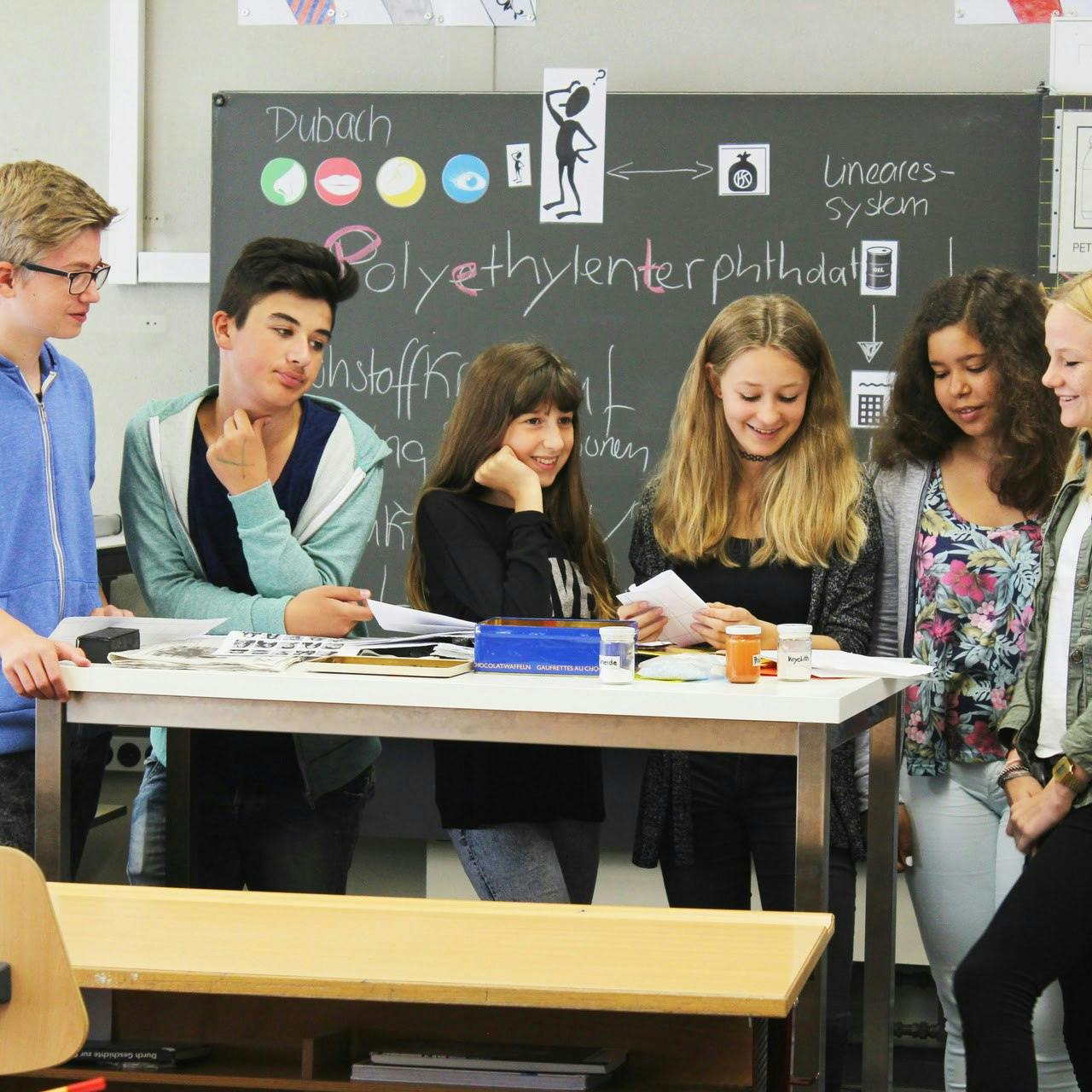 Sechs Jugendliche stehen um einen Tisch in einem Klassenzimmer. Transformatives Lernen passiert in einem sicheren Raum wie dem Klassenzimmer und bietet die Möglichkeit für gemeinsames Lernen für nachhaltige Entwicklung.